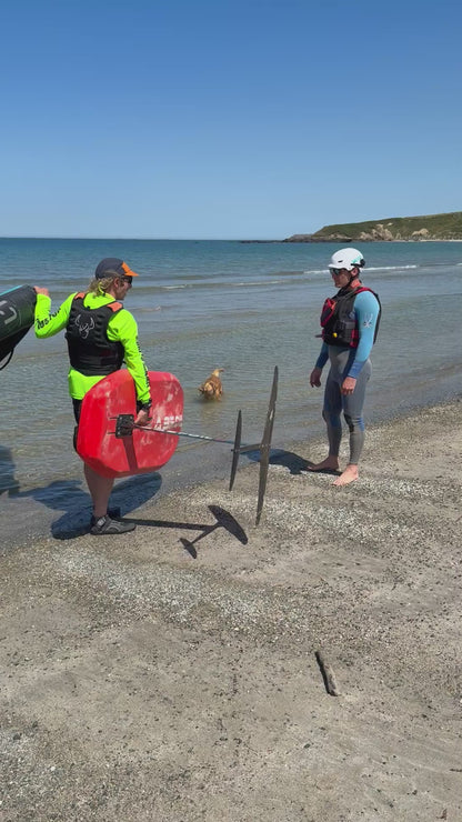 Surf to summer instructor demonstrating beach access whilst carrying equipment hard to Foil Wing  North Wales crystal clear Kite Foil and tow Foil conditions